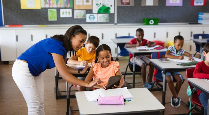 African american female teacher teaching disabled girl to use digital tablet at elementary school. school and education concept