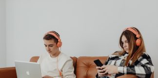 two teens with headphones on, one on the computer the other on their phone; internet safety