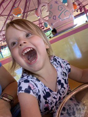 little girl yelling in yellow ride care with teapot behind her