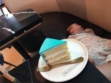 piece of cake with teal icing on white plate with baby asleep