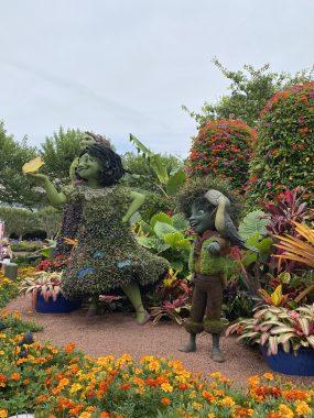 Encanto's Mirabel and Antonio made of flowers in front of trees and Spaceship Earth