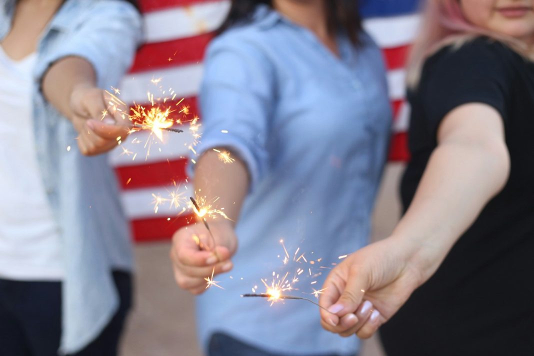 10 tip for a safe Fourth of July Alondra Olivas via Unsplash three women hold sparklers with an American flag behind them