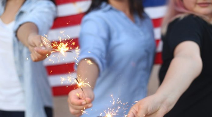 Central Florida 4th of July Celebration Guide Alondra Olivas via Unsplash three women hold sparklers with an American flag behind them