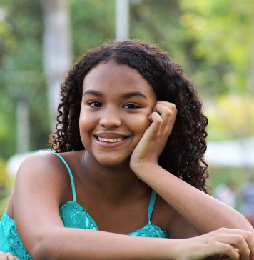 Dark brown girl teen with dark hair smiling and staring into the camera.