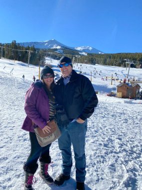 couple dressed for the cold on a snowy ski resort smiling at the camera. travel with your partner