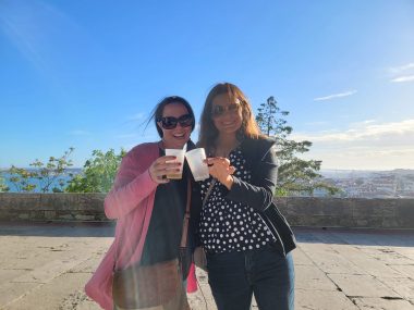 two women smiling at the camera, chicking their glasses together. girls trip