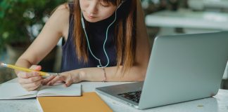 Navigating the College Admissions Process: A Comprehensive Guide for Moms girl writing in notebook with earbuds and a computer in front of her, going through college asmission