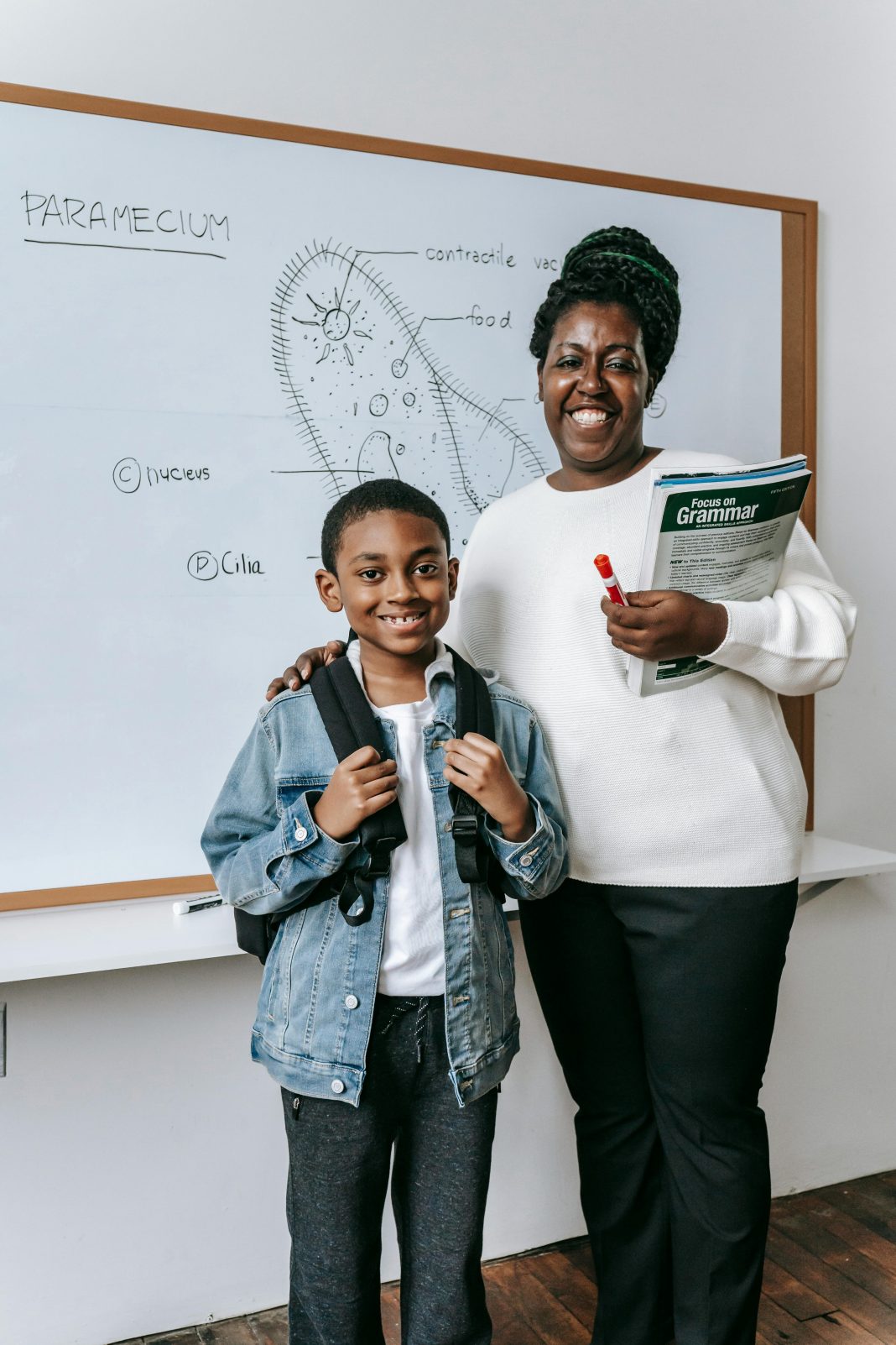 woman and child standing in front of a white board with a science lesson on it smiling at the camera. All to help kids thrive at school