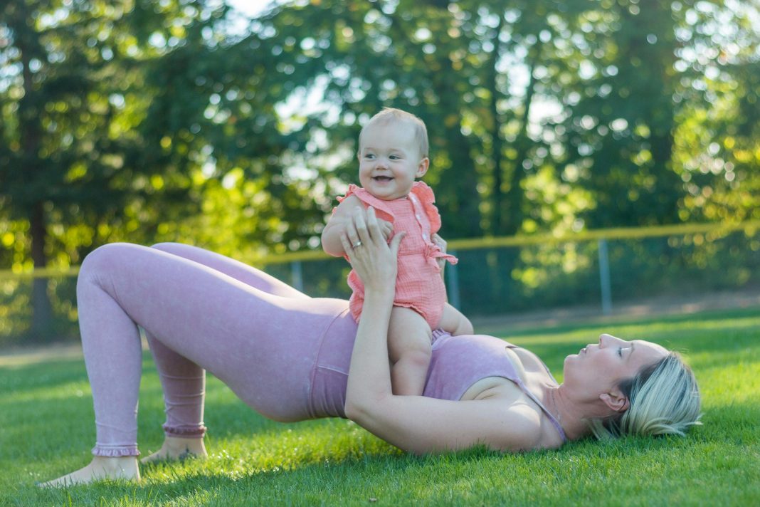 mom in workout clothes outside with baby on top of her, working out together finding gyms with childcare