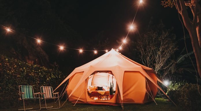 a tent outside lit up from within and string lights overtop for backyard camping