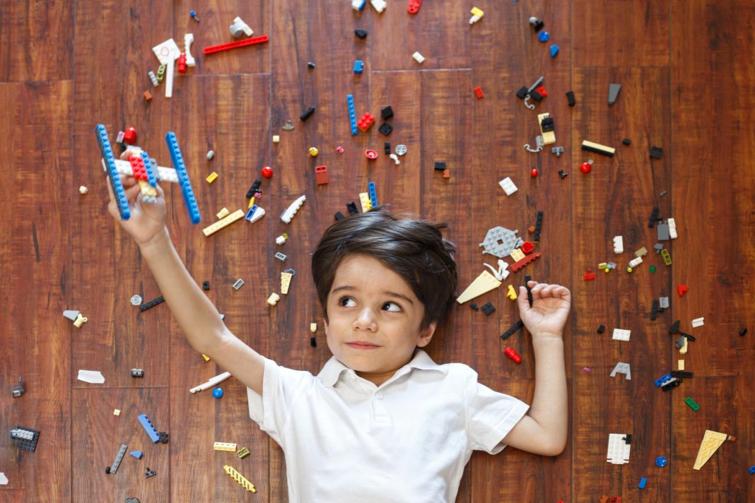 Little boy on floor with legos around him and a makeshift lego plane in one hand, flying with kids.