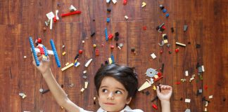 Little boy on floor with legos around him and a makeshift lego plane in one hand, flying with kids.