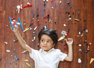 Little boy on floor with legos around him and a makeshift lego plane in one hand, flying with kids.