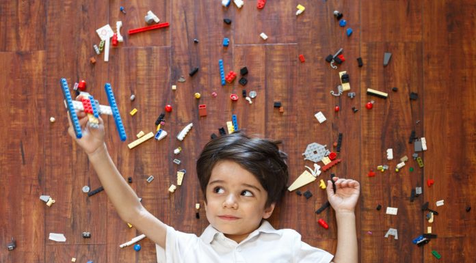 Little boy on floor with legos around him and a makeshift lego plane in one hand, flying with kids.