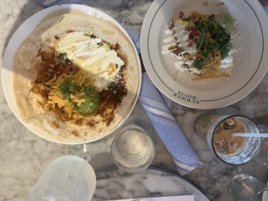 Two breakfast dishes, iced coffee, and water on a marble table during Mother's Day brunch.