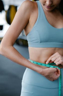 body of woman wearing workout clothes measuring her waist