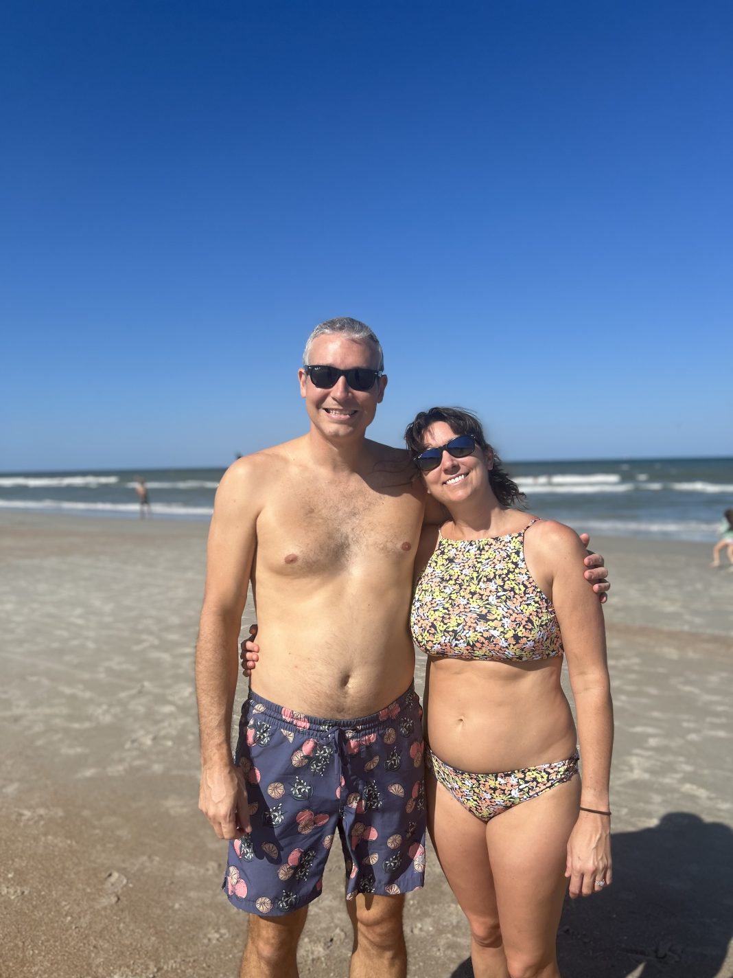 man and woman in bathing suits at the beach smiling at the camera