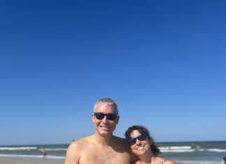 man and woman in bathing suits at the beach smiling at the camera