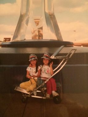 two young girls in a stroller-looking device staring and smiling at camera. Old picture