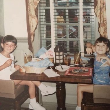 Two young girls smiling at camera sitting at a table. old picture.