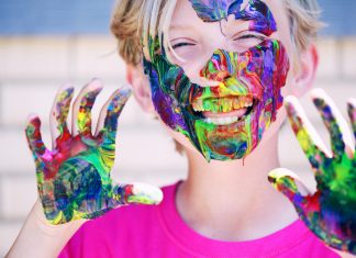 child laughing at camera with colorful paint on hands and all over face, educational resources