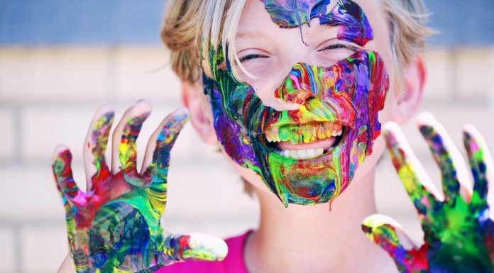 child laughing at camera with colorful paint on hands and all over face, educational resources