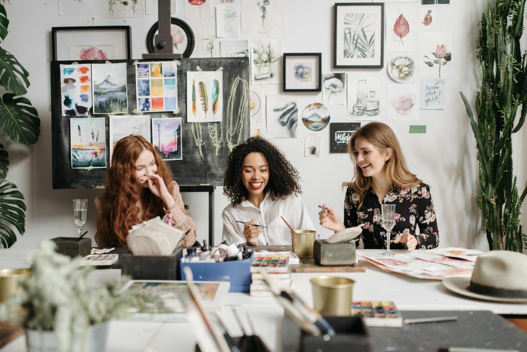 three women staring at a painting and smiling and laughing.