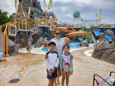 two kids and mom smiling in front of a water park