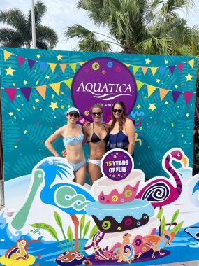 three women in bikinis in front of purple Aquatic sign