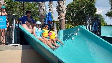 a man, woman and two kids sitting side by side at the top of a water slide