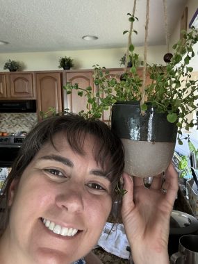 woman smiling at camera lifting a plant by her head. 