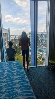 two young children, one boy and one girl, looking at their window to the pool from their hotel room for a staycation at Cabana Bay, Orlando, FL