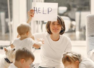 mom holding up a sign that says "help," with children around on her with school supplies for back to school madness