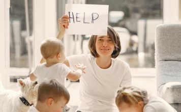 mom holding up a sign that says "help," with children around on her with school supplies for back to school madness