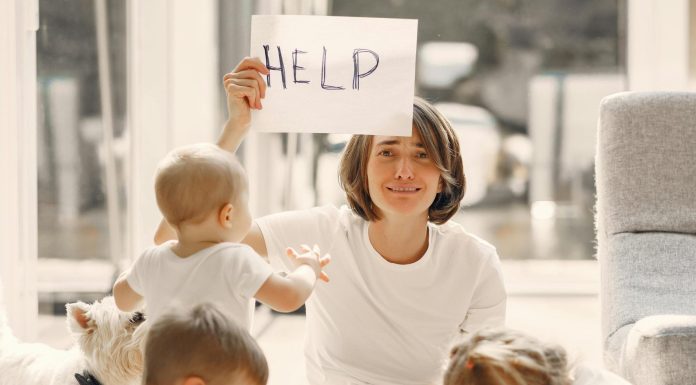 mom holding up a sign that says "help," with children around on her with school supplies for back to school madness