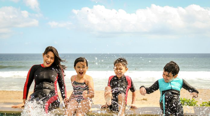 A mom and her three children smiling and splashing water wearing wetsuits sitting on a dock.