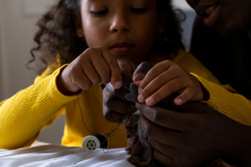 introducing kids to sewing: a young girl sewing a stuffed animal with parent