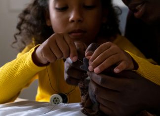 introducing kids to sewing: a young girl sewing a stuffed animal with parent