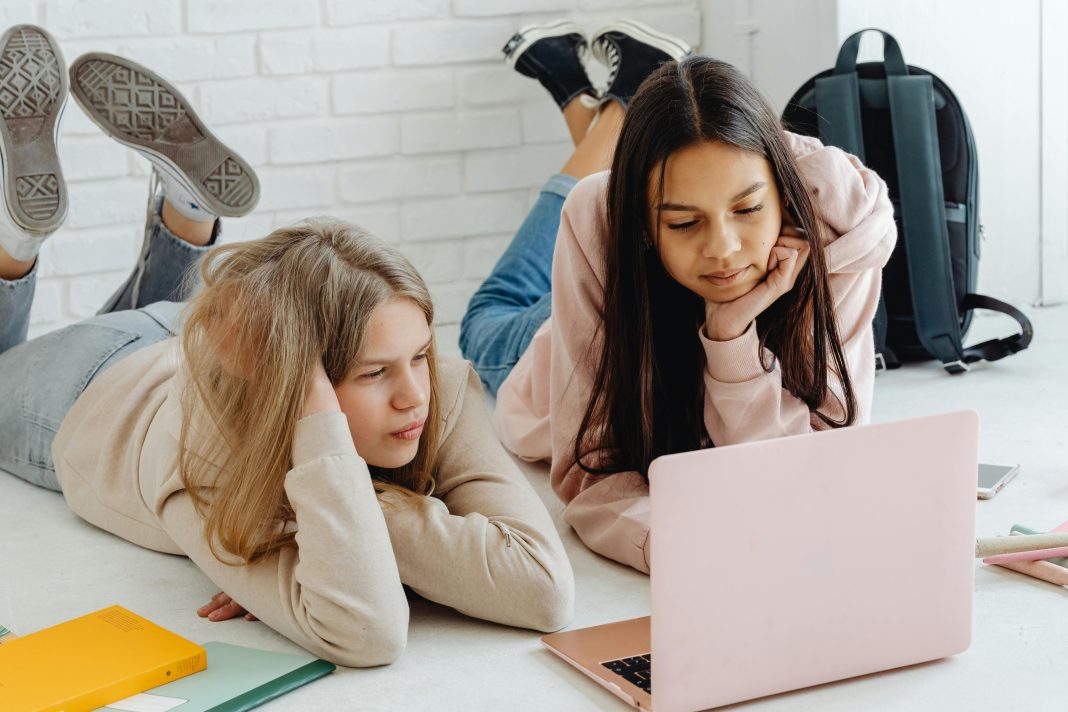 two girls laying down on the ground looking at a laptop transition to high school