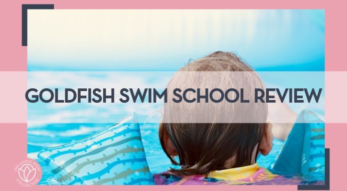 the back of a child's head in a pool with blue and green striped floats on their arms with words 'goldfish swim school review' overtop