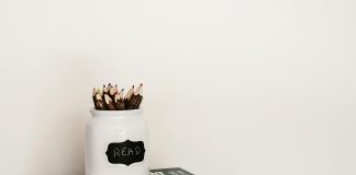 stack of books with a pencil jar on the top against a white wall