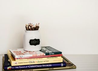 stack of books with a pencil jar on the top against a white wall