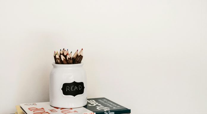 stack of books with a pencil jar on the top against a white wall