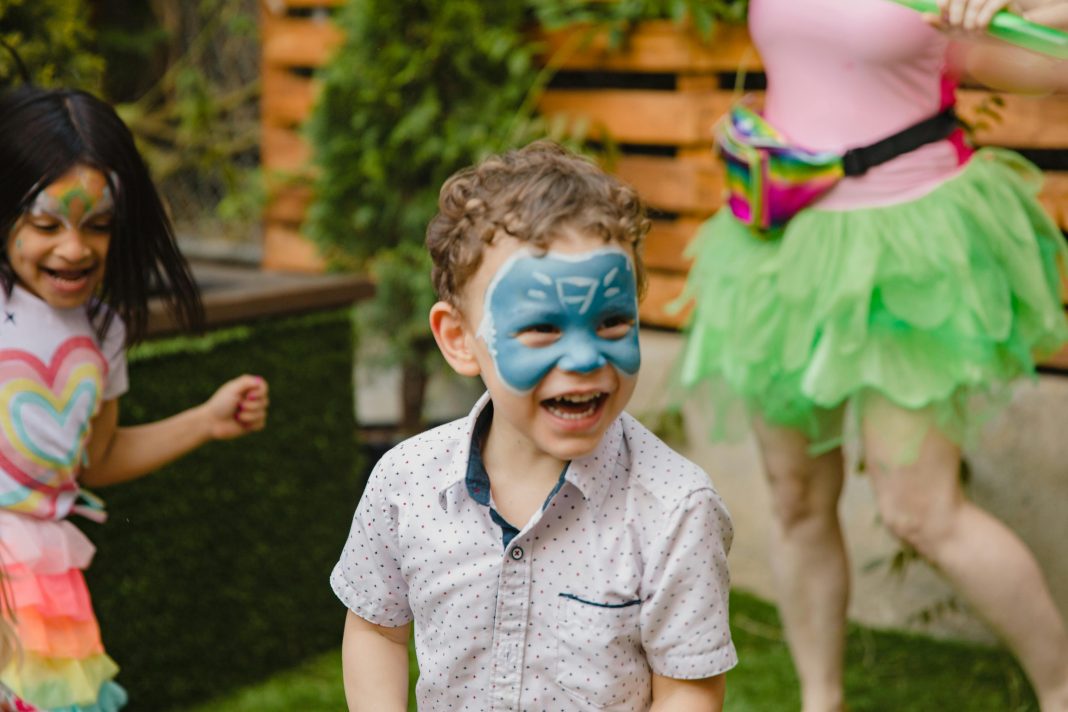 a young by with a painted face smiling look off to the side from the camera, for a safe and fun playdate ideas