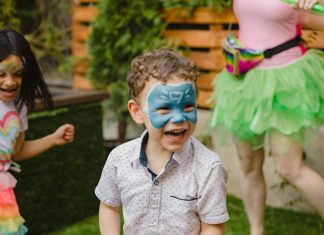 a young by with a painted face smiling look off to the side from the camera, for a safe and fun playdate ideas