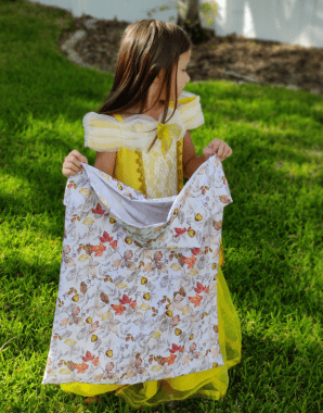 young girl in belle costume looking away from camera holding up the finished pillowcase ill use as a trick-or-treat bag. 