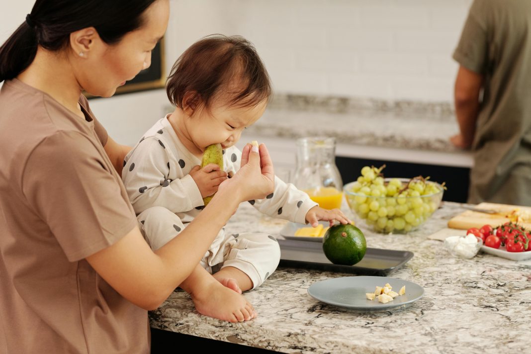 child on kitchen counter eating avocados with mom