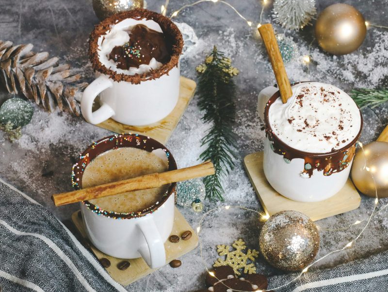 three cups of hot chocolate with white mugs with Christmas items on table below them