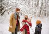 a family, husband, wife, two young children laughing and playing in the snow while trying to take picture; winter health tips for moms