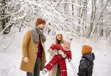 a family, husband, wife, two young children laughing and playing in the snow while trying to take picture; winter health tips for moms